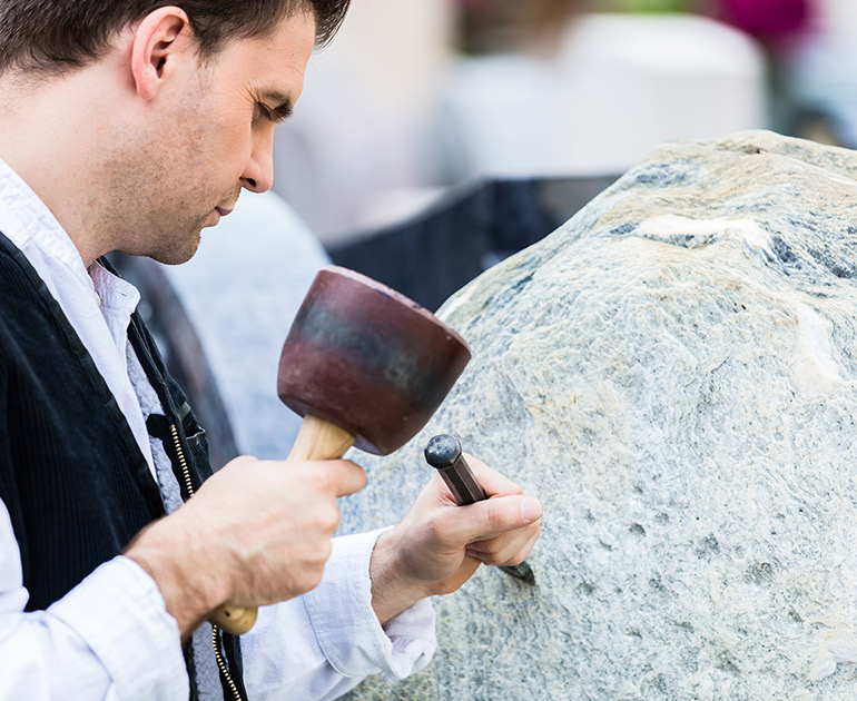 Ein Steinmetz bearbeitet mit einem Meißel einen Granitblock